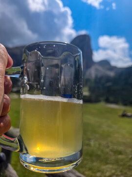 Hand held Radler beer mug raised against a bright mountain landscape and blue sky, conveying summer relaxation, refreshment and outdoor leisure in an alpine meadow setting during a sunny day.