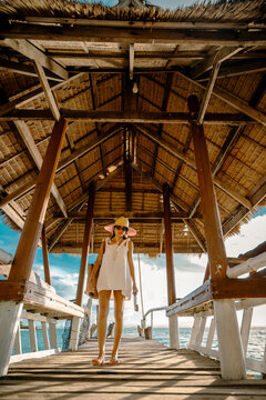 Woman tourist stay on balcony of the hut lap into the sea, relax moment on wooden pier, enjoy sunset of the summer trip in tropical island