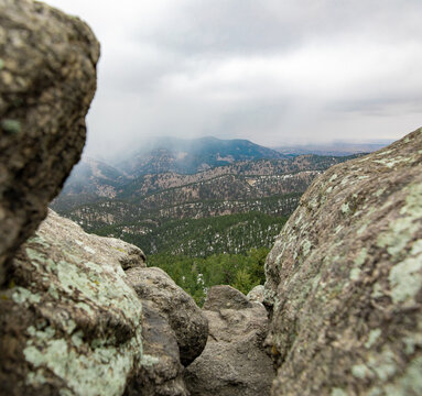 Broomfield, Colorado, United States - 22 March 2026: View of a mountain landscape framed by rocky outcrops with pine forests and cloudy skies.