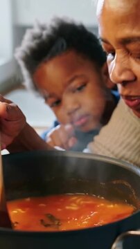 Vertical video: Steam urging grandma in knit stirring testing heat at home, with spoon kid watching