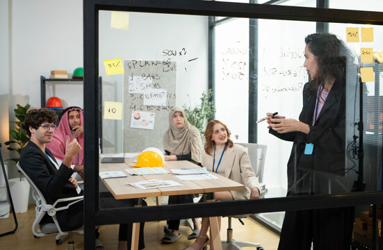 Businesswoman writing project plans on a glass board during a business meeting in a modern office,