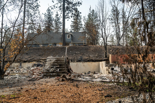 Spokane, Washington, United States - 14 August 2026: View of the aftermath of the 2026 Spokane wildfires, showing a house foundation and charred trees in a residential area.