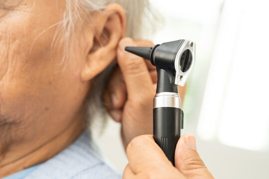 Audiologist or ENT doctor use otoscope checking ear of asian senior woman patient treating hearing loss problem.