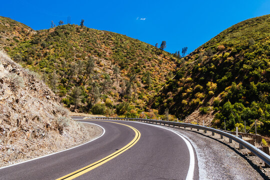Asphalt road winds through dry chaparral hills in California
