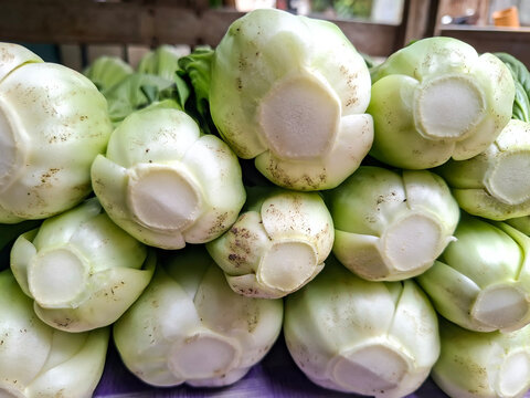 close-up view of fresh bok choy cabbages stacked together, highlighting their thick, smooth white stems and base roots.