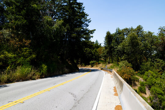 Winding asphalt road with double yellow lines through forest, California USA.
