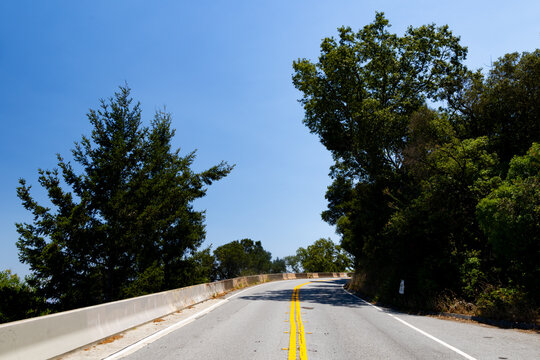 Asphalt road curves through densely forested hills under a clear blue sky in California