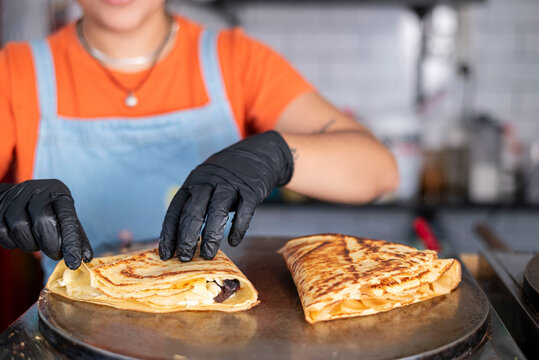 Preparing fresh crepes with gloves on hot griddle