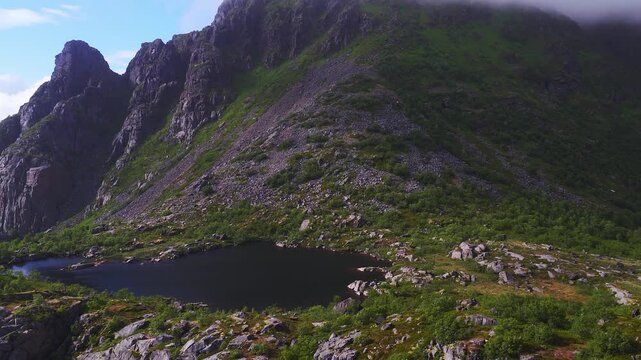 Aerial video flying over a rocky mountain ridge, alpine lake, and steep scree slopes in the Lofoten archipelago in Norway during daytime.
