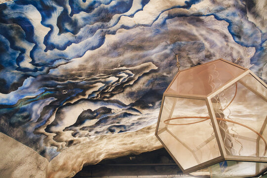 Stockholm, Sweden - 05 August 2026: View of the artistic ceiling mural at T-Centralen subway station, featuring swirling blue and white patterns, illuminated by a geometric glass lantern.