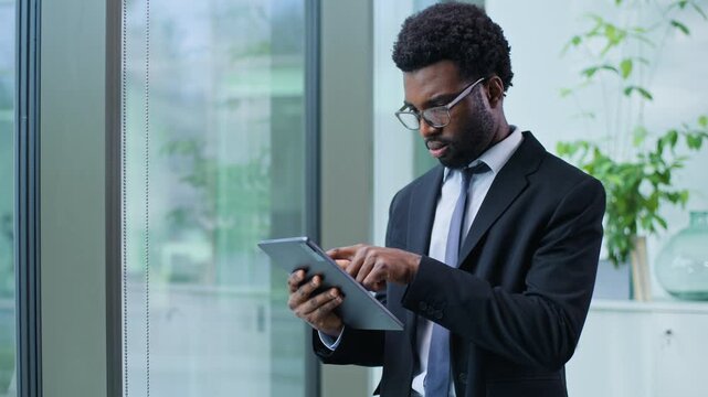 Serious African American business man concentrated browsing digital tablet working with internet work ethnic businessman male guy with technology corporate cyberspace agent using gadget in office