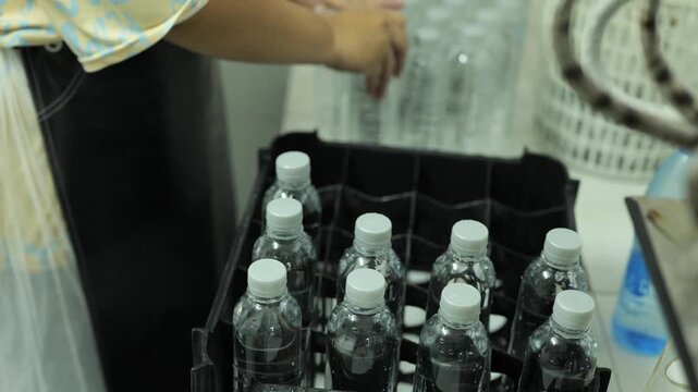 Hand inspecting rows of sealed drinking water bottles on a manual production line in a small-scale water bottling factory, workers checking quality before packaging, local water bottling small busines