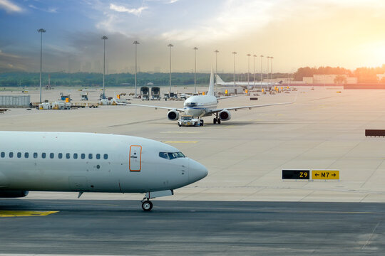 Commercial airliners move slowly on the taxiway at a large airport terminal during the golden hour as ground crews prepare for upcoming evening departures