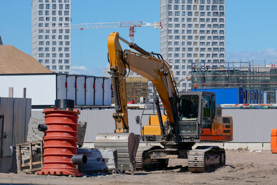 Large construction machinery operates at a busy site during the day near unfinished high rise apartment buildings and piles of earth materials