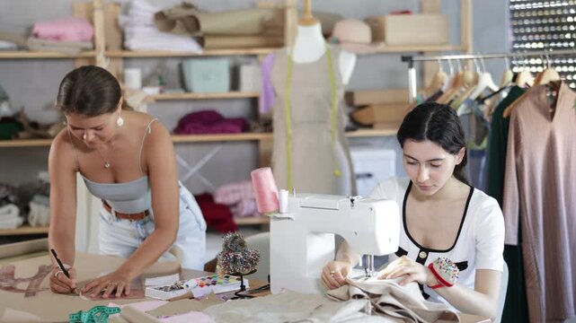 Young seamstresses stitching and drafting paper patterns in workshop