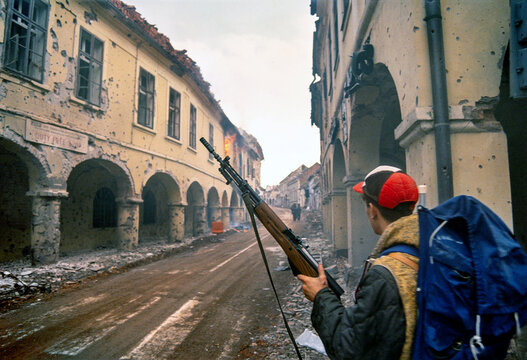 Vukovar, Croatia - 18 November 1991: View of a Serbian fighter carrying a rifle walks through a war-torn street on the final day of the Battle of Vukovar, amid heavily damaged buildings.