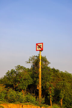 Kampong Phluk, Siem Reap Province, Cambodia - 05 February 2020: View of a warning sign on a pole near the Tonle Sap lake, surrounded by lush green trees under a clear blue sky.