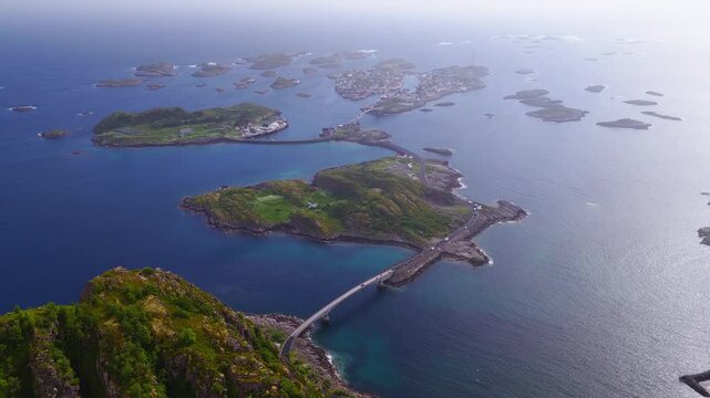 An aerial panorama shows the bridges connecting small rocky islands leading toward Henningsvaer fishing village in Lofoten, Norway on a clear day.