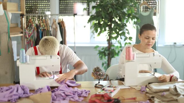 Tailors are working on a collection of clothes. Male tailor working in team with Asian female seamstresses, they sew the sample for approval with customer . High quality 4k footage