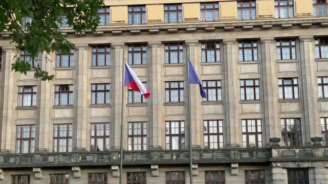 two flags on slender poles move softly before stone neoclassical facade with symmetrical tall windows, pilasters and carved details under calm diffuse daylight flag
