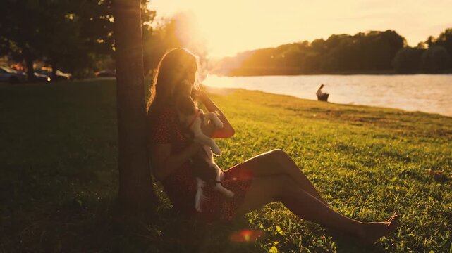 Girl leans against a tree trunk with a spaniel puppy at sunset