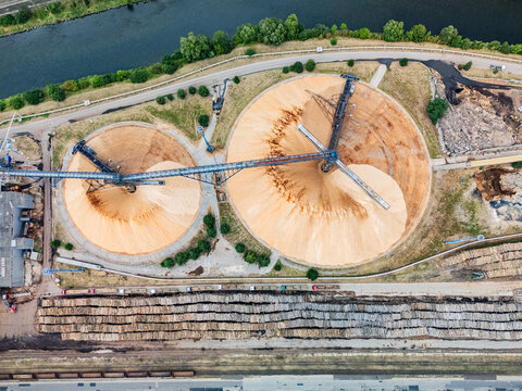 Aerial view of the Mondi SCP factory featuring large circular wood chip storage piles, industrial conveyor systems, and timber logs in Ruzomberok, Zilinsky kraj, Slovakia.