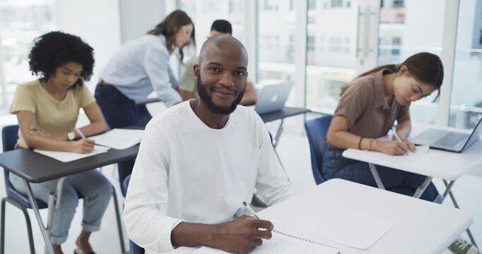 Students, writing and desk in lecture at university for learning, education or knowledge with scholarship. Young man, notebook and study with book at college for test, exam or assessment with smile