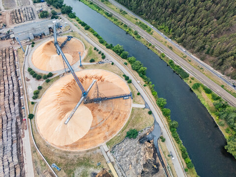 Aerial view of Mondi SCP factory with large wood chip piles, conveyor systems, river, and railway line in Ruzomberok, Zilinsky kraj, Slovakia.