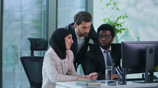 Multiethnic business team three colleagues discussing talking looking in computer together in office Caucasian leader boss help advise talk helping Muslim woman and African American man with work