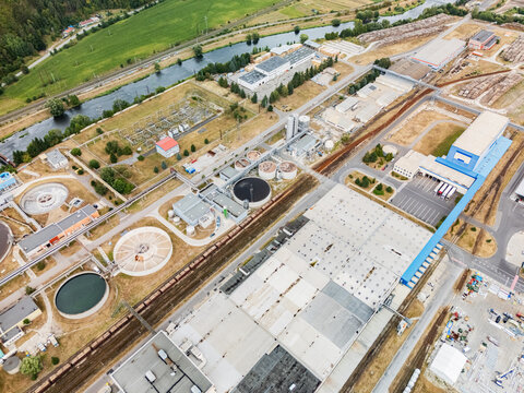 Aerial view of the Mondi SCP factory complex featuring industrial warehouses, circular water treatment tanks, and railway tracks near the river in Ruzomberok, Zilinsky kraj, Slovakia.