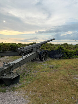Historic 155mm GPF artillery gun stands among coastal dunes beneath a dramatic evening sky at Fort Macon State Park in Atlantic Beach, North Carolina.