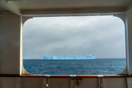 Antarctica: view from the porthole of a ship at sea, framing an impressive tabular iceberg.