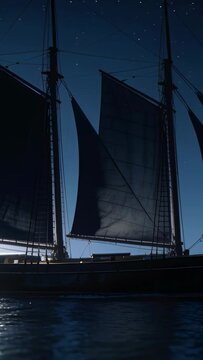 Vertical video: Sailing two-masted schooner moving slowly across night sea, breeze filling sails