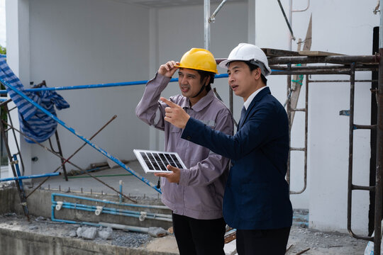 Construction engineer and client reviewing a solar panel at a residential building site, discussing renewable energy solutions, project planning, quality, sustainable construction and site management.