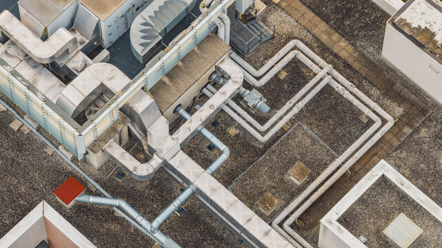 Aerial view of industrial rooftop ventilation ducts, insulated pipes and HVAC infrastructure forming geometric patterns on a large building, Valence, Auvergne-Rhone-Alpes, France.