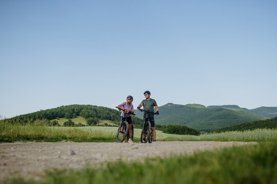 Senior couple taking break during e-bike ride, enjoying nature around them.