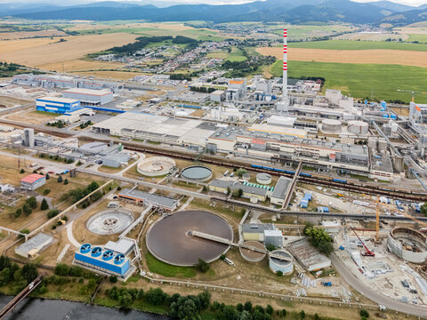 Aerial view of Mondi SCP factory featuring industrial buildings, large circular water treatment tanks, and a tall chimney in Ruzomberok, Zilinsky kraj, Slovakia.