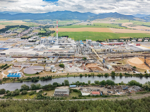 Aerial view of the Mondi SCP factory featuring industrial buildings, a tall chimney, wood chip piles, and the Vah River flowing through the landscape in Ruzomberok, Zilinsky kraj, Slovakia.