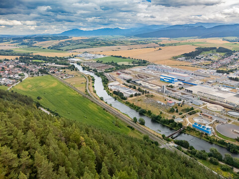 Aerial view of the Mondi SCP factory complex situated along the river with surrounding green fields, forests, and distant mountains in Ruzomberok, Zilinsky kraj, Slovakia.