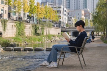 Fototapeta premium Young Man Reading a Book Outdoors Beside an Urban Stream
