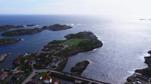 Aerial view reveals the iconic Henningsvaer football stadium surrounded by the Norwegian Sea, rocky islets, and coastal buildings in Lofoten, Norway.