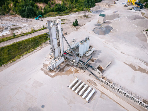 Aerial view of a concrete production facility featuring tall silos, conveyor belts, and a row of white liquefied petroleum gas tanks situated in an industrial area in Latvia.