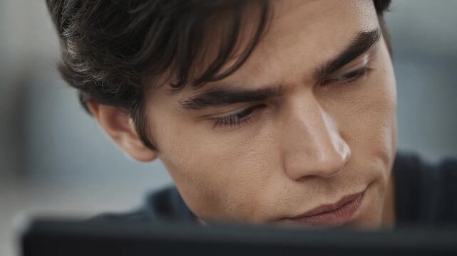 Focused young programmer coding on computer, handsome man looking at monitor with concentration, extreme close up of face