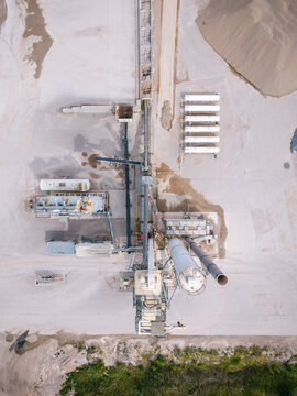 Aerial view of an industrial concrete production facility featuring a series of LPG storage tanks, conveyor belts, and gravel piles in Mundigciems, Talsi Municipality, Latvia.