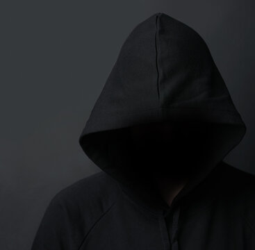 Dark, hoodie and hacker in studio, hiding and undercover for stalking, person and thief with crime. Black background, scam and criminal with danger, burglary and creepy in shadows, villain and fraud