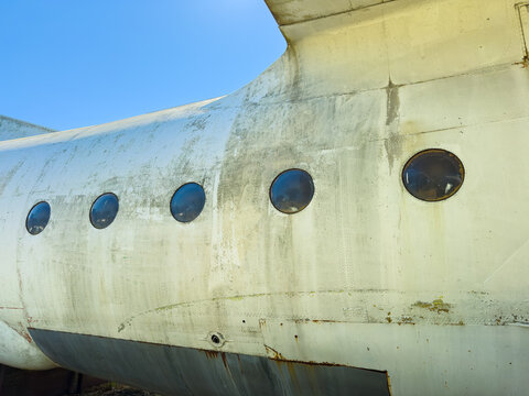 Close view of old airplane fuselage showing windows and weathered surface in a clear blue sky during daytime