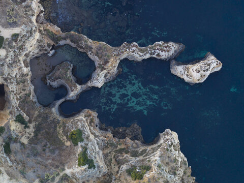 Aerial view of rugged limestone cliffs and turquoise sea coves along the coastline of Portugal.