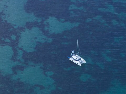Aerial view of a catamaran sailing in clear turquoise waters off the coast of Portugal.