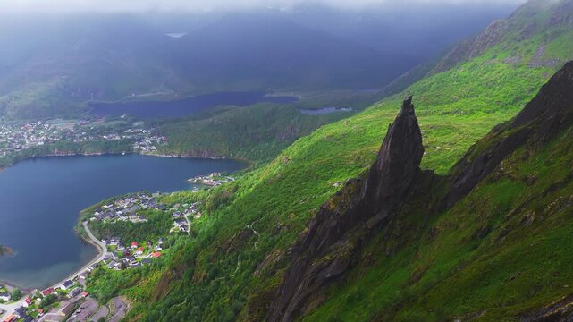 An aerial flight past the famous Svolvaergeita rock pinnacle on the steep mountain slope above the coastal town of Svolvaer, Lofoten, Norway.