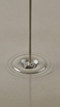 Smooth Stream of Creamy Grey Liquid Pouring into Pool creating Concentric Ripples